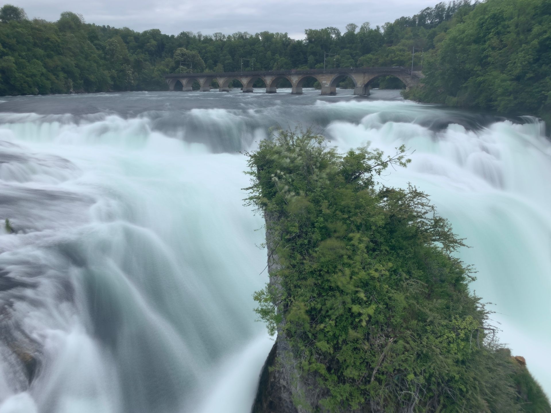 Long-exposure of the Rhine Falls with a moss-covered green rock in the foreground