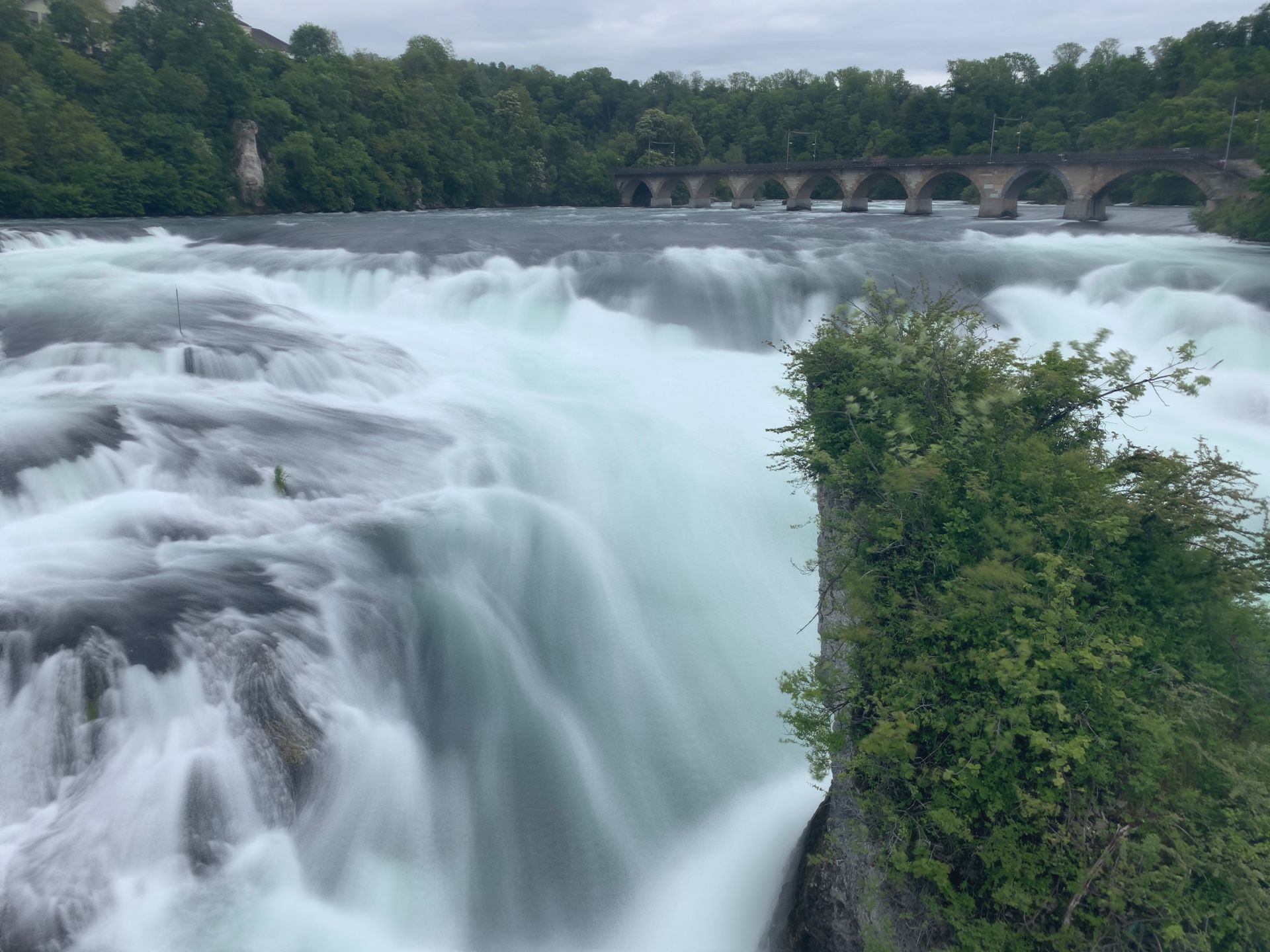 Wide curtain of the Rhine Falls with the old stone arch bridge visible in the background