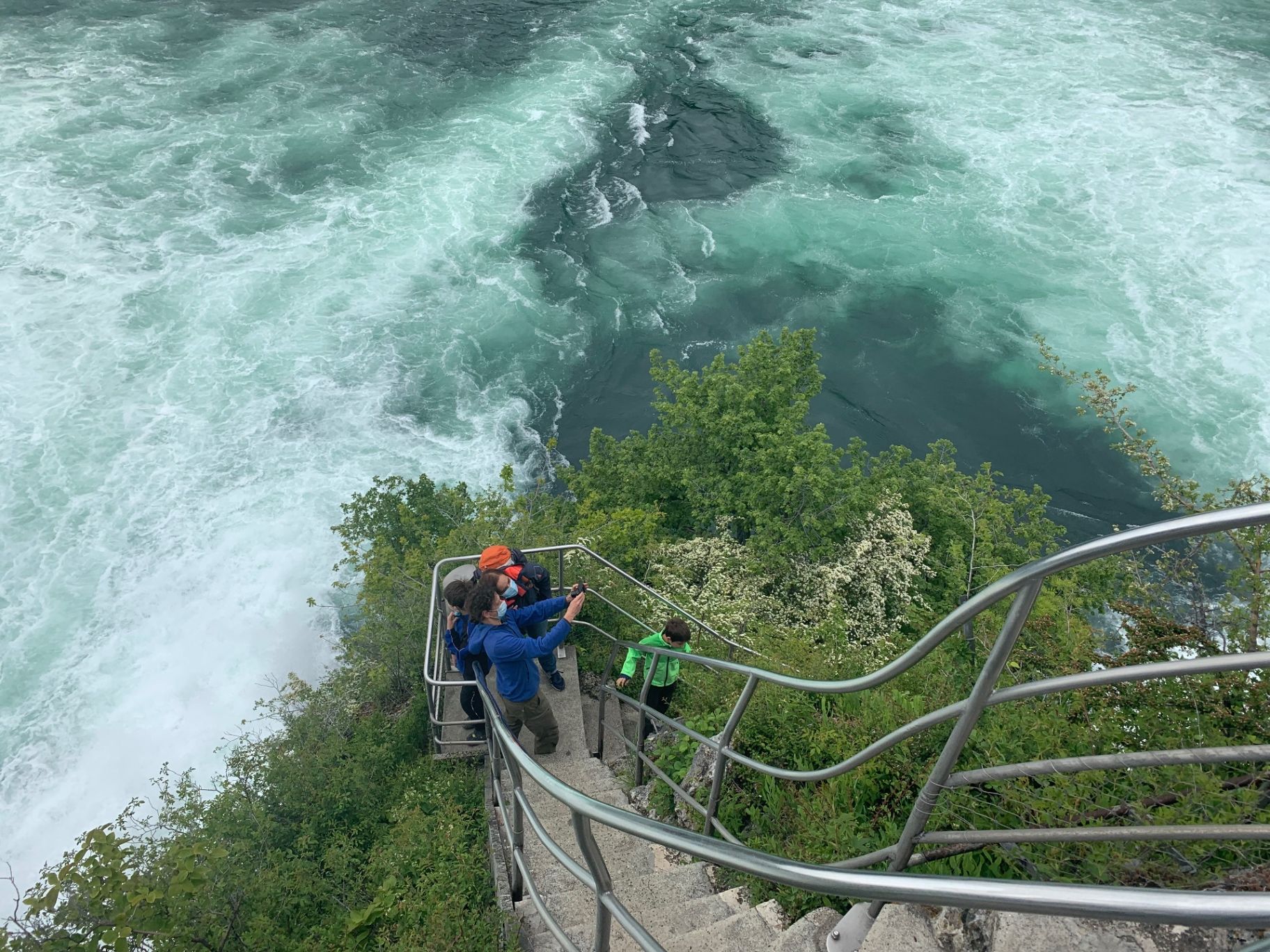 Visitors on the metal viewing deck looking down at the turquoise rapids below the falls