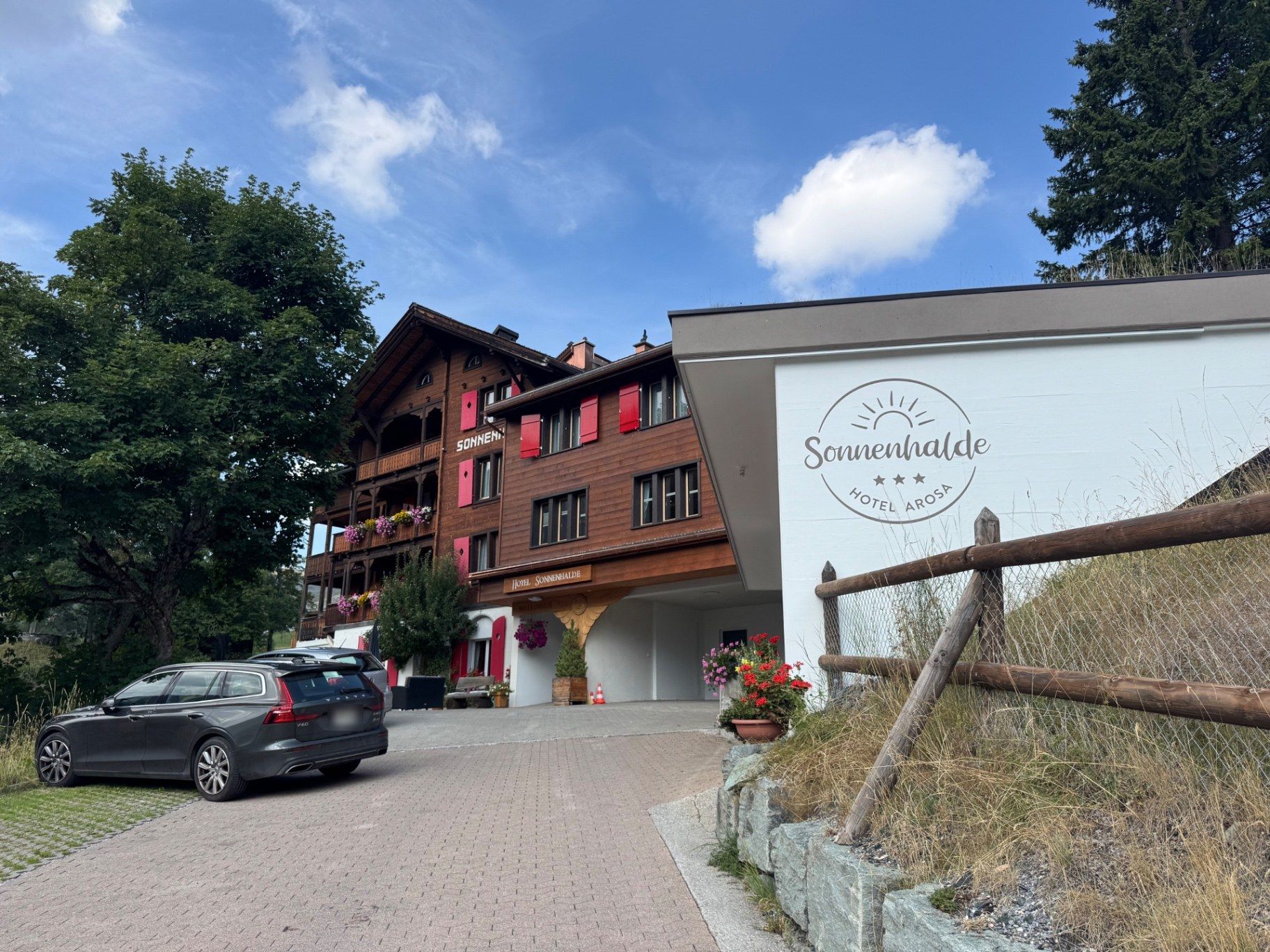 Hotel Sonnenhalde in Arosa: a timber chalet with red shutters, flower boxes and a sun-motif logo