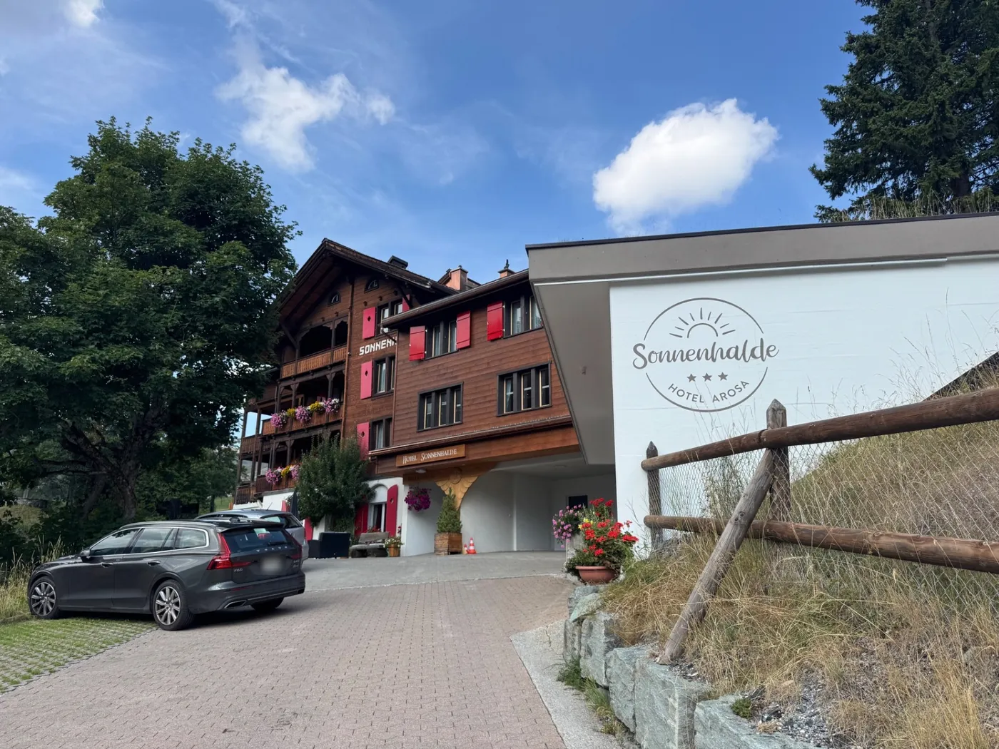 Hotel Sonnenhalde in Arosa: a timber chalet with red shutters, flower boxes and a sun-motif logo