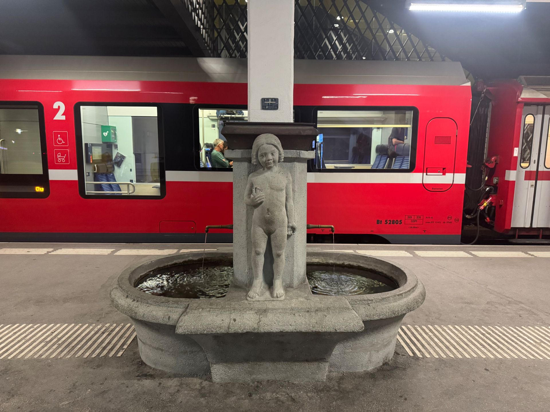 The red Rhaetian Railway train at Arosa station, with the old stone platform fountain