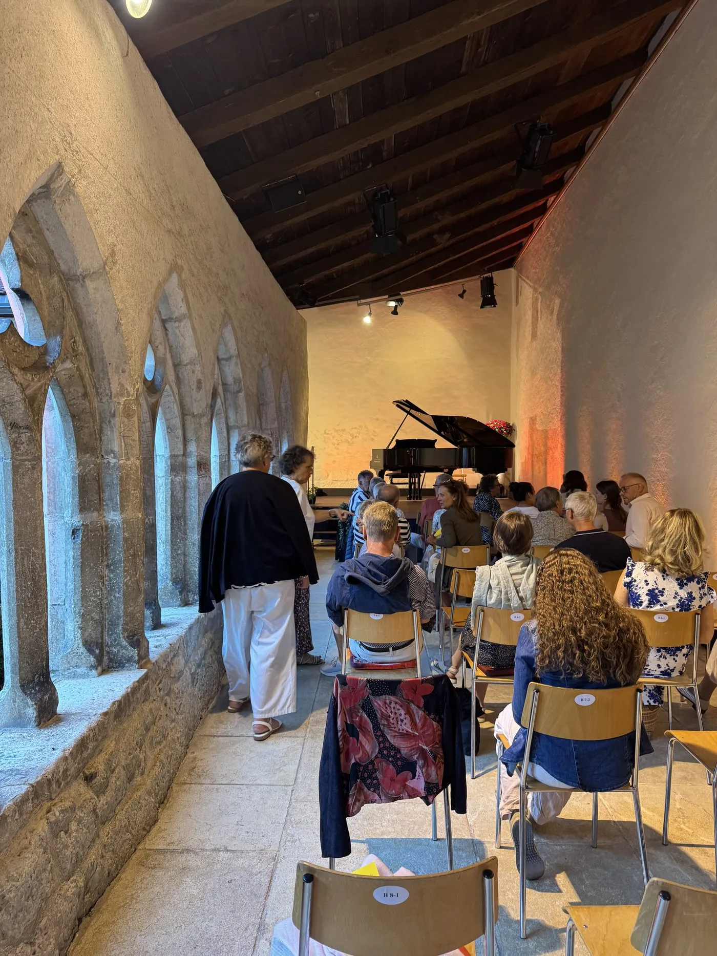 A grand piano set up in the vaulted cloister gallery with the audience seated